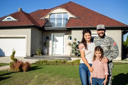 An army soldier stands outside a home with his wife and daughter
