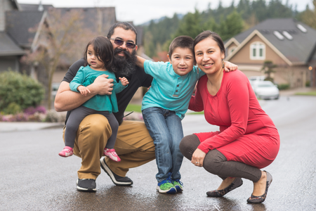 A Native American man and woman crouch smiling in the road outside a home with a young girl and boy.