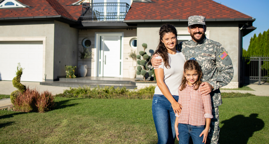 An army soldier stands outside a home with his wife and daughter